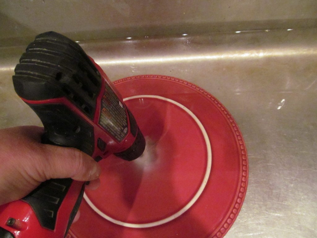 photo of drilling a hole through a plate with a cordless drill while the plate in in the sink under a little bit of water.