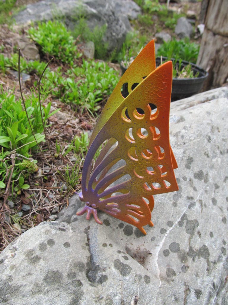 Trash to treasure. A metal butterfly has been spray-painted bright colors. It sits on a rock in the garden