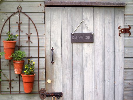 Garden Sheds. Picture is a close up of a wood plank shed door with a little sign hanging on it that says "Garden shed". Hanging on the wall next to door are flower pots.