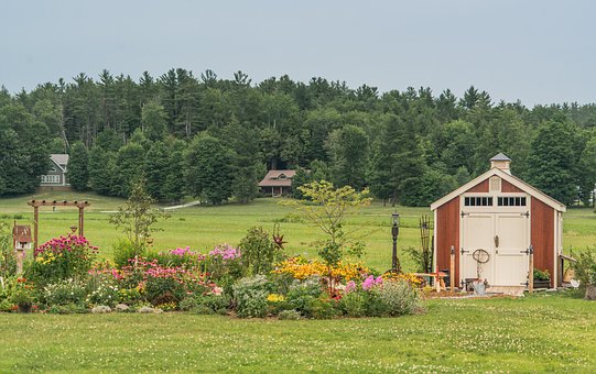Garden sheds. The picture is of a shed on a very large property with big lawn. The shed is bordered by a long row of showy flowers and small shrubs