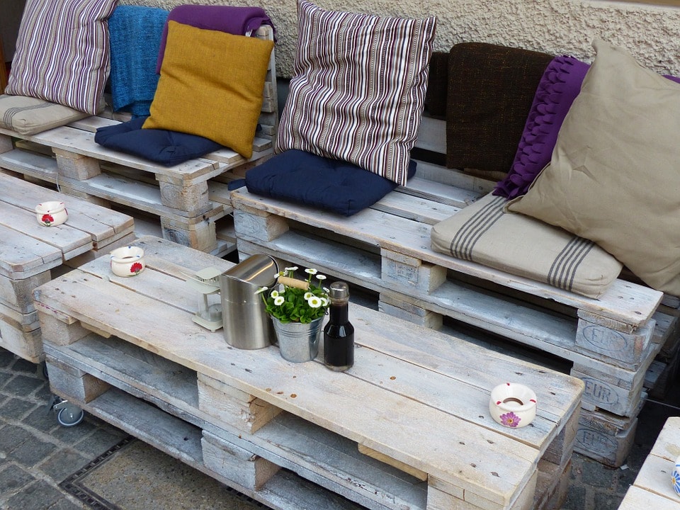 outdoor seating made by stacking 3 shipping pallets one on top of another with a back rest. There are decorative pillows for comfort.
