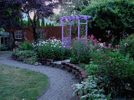 casual cottage garden theme with a gravel pathway, lots of tall flowers and a purple arbor in the center.