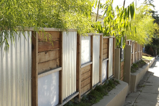 Modern style fence that uses re-cycled pallet board and shiny corrugated metal sheets in an attractive square and rectangle pattern.