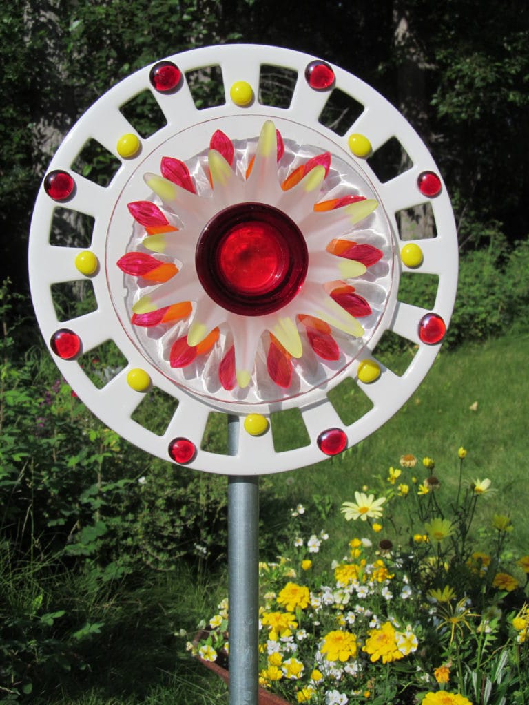 Best Dish Flowers with a ceramic plate that looks kind of like a car hub cap. It has been decorated brilliant red and yellow like the sun