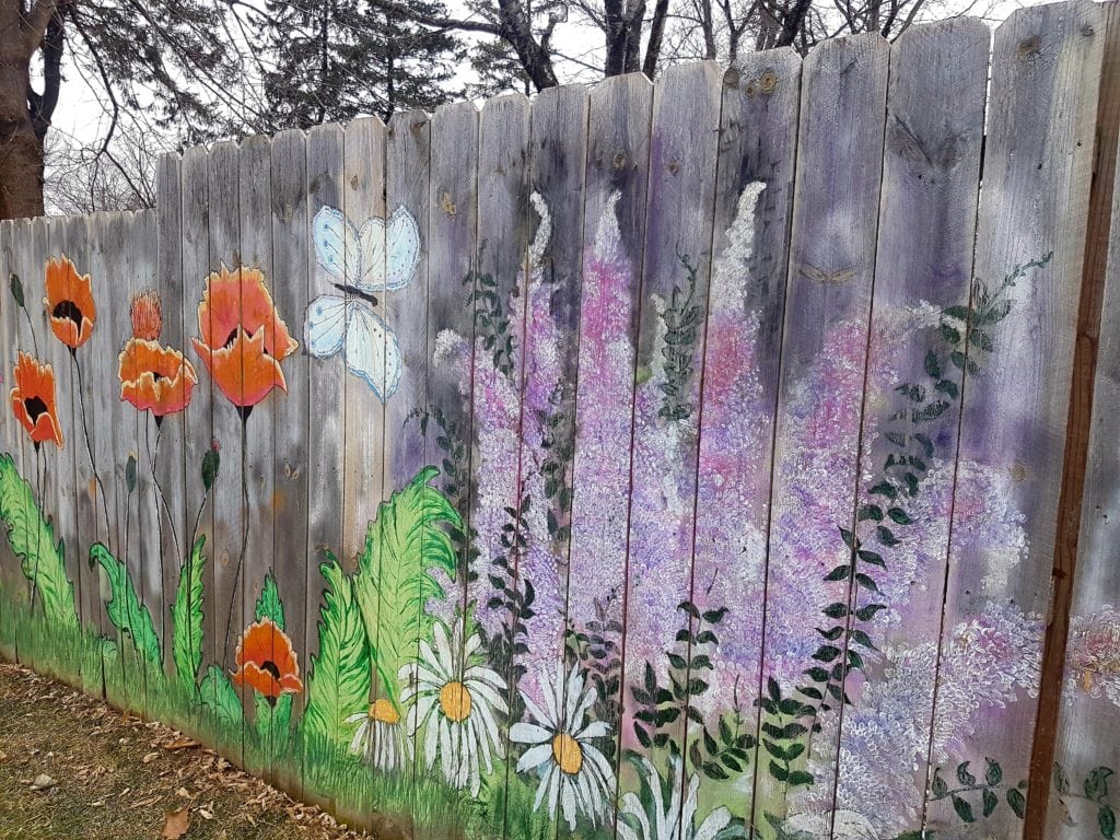 wooden fence with a large colorful mural of flowers, ferns and butterfly on it.