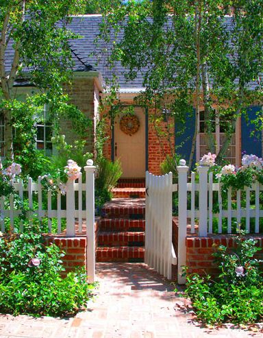 Fences in your landscape, a pretty suburban single story ranch-style house front yard has a white picket fence in front of it.  Gate is open to the walkway leading to front door.