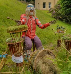 Scarecrow dressed like a hippy playing the drums in front of someone's house.