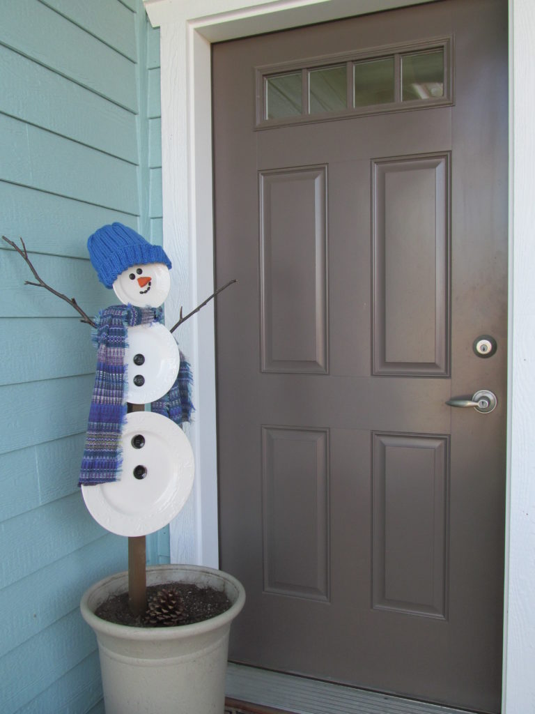 photo of a snowman plant stake made from dishes. It's on the front porch as a holiday decoration