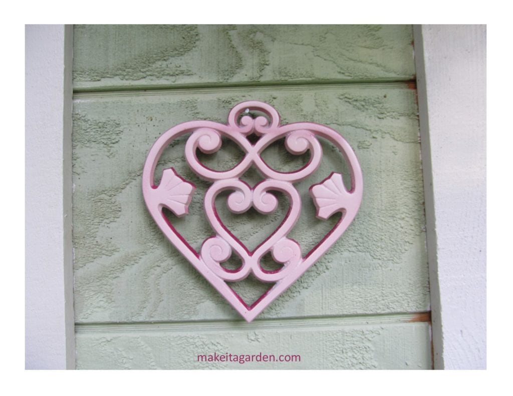 a cast iron heart-shaped trivet hangs on the wall of the garden shed
