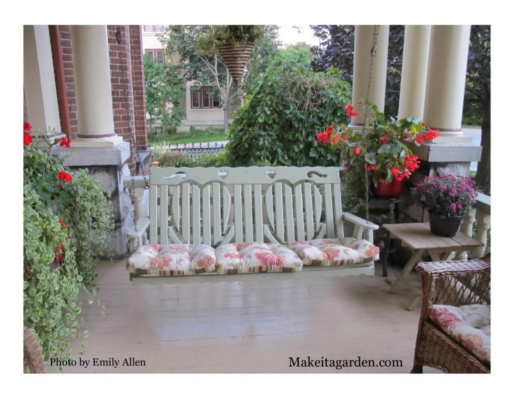 Pretty decorative porch swing under the front porch with flowers around it.