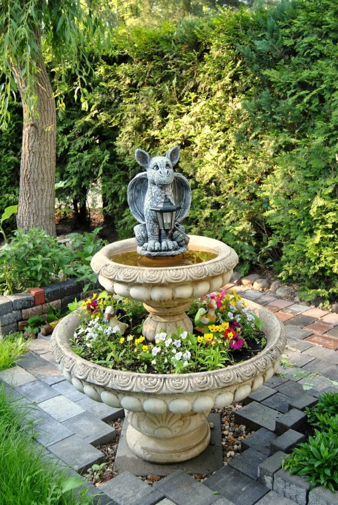 Large fountain turned into a planter with lots of flowers and a statue on top