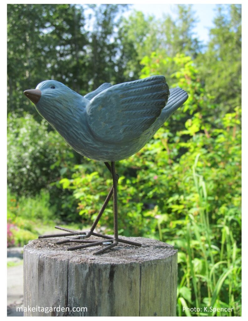 Trash to treasure. A votive candle holder is shaped like a little blue bird. It sits on a fence post in the garden