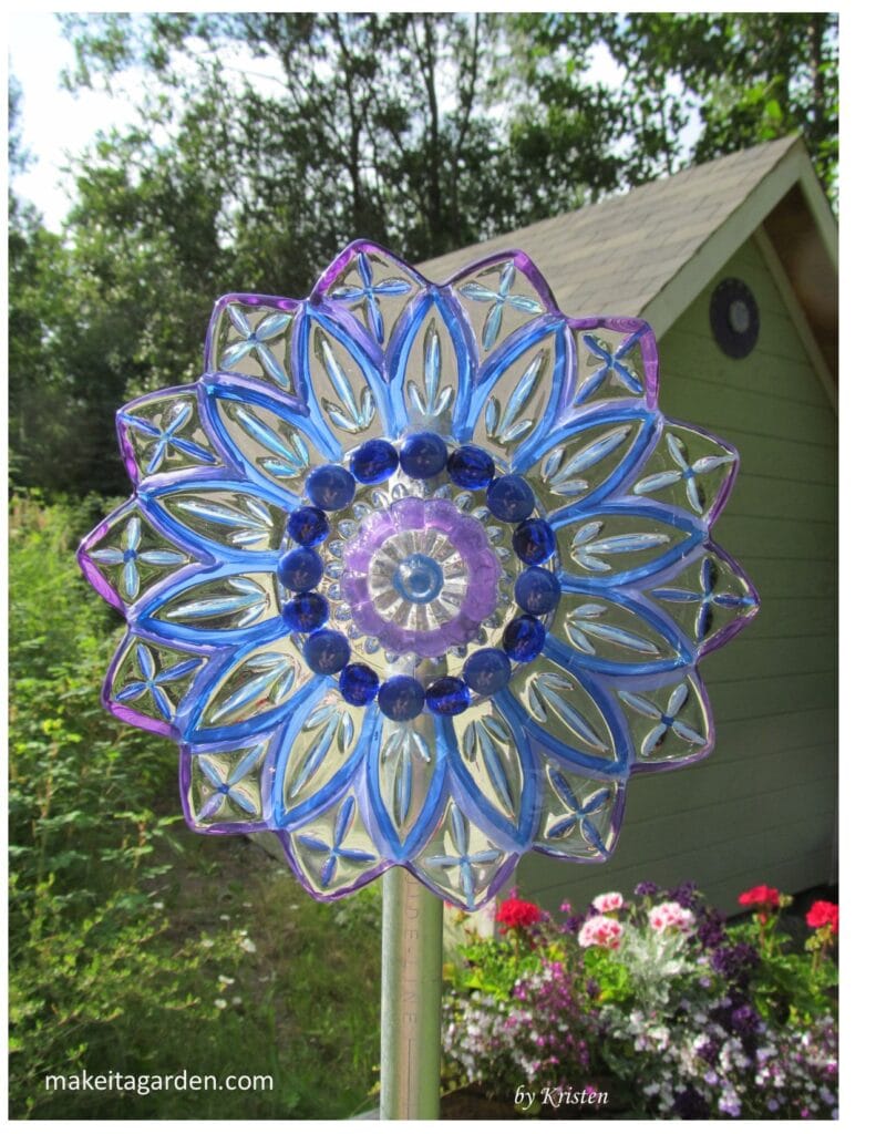 Dish flower made from a clear glass plate an painted bright colors to look like a flower. It's pictured outside in the artist's garden