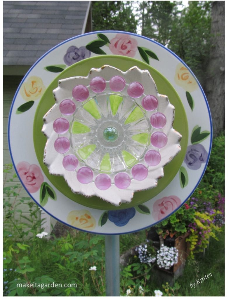 plate flowers a dish flower garden ornament made by the artist. It stands upright on a post in the garden.  It has bright colors and a more modern pattern