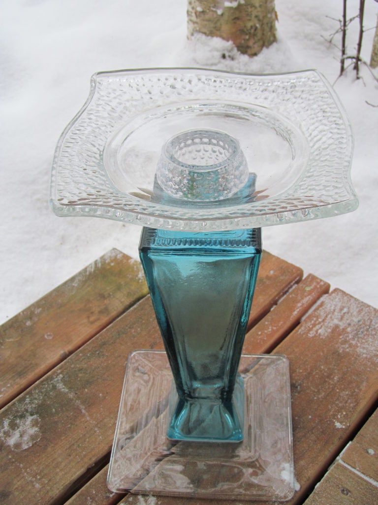 a plant stand made from a tall blue colored glass vase turned upside-down with a clear plate on top 