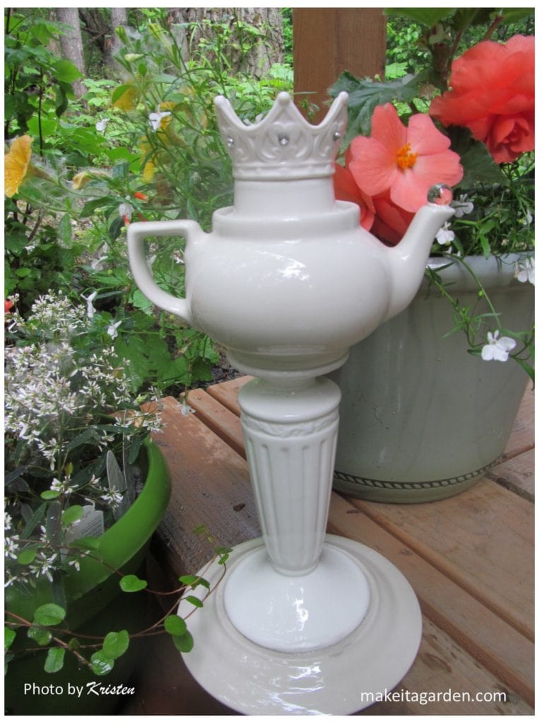 A garden totem made with all white dishes comprised of candle pillar, teapot and decorative votive candle holder in the shape of a crown.