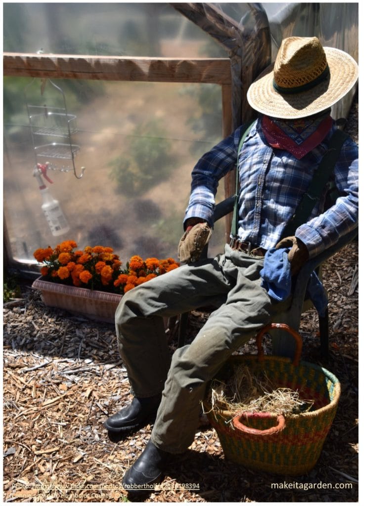 Garden Scarecrow dressed to look like a cowboy leans against bale of straw. Country Cottage garden ideas
