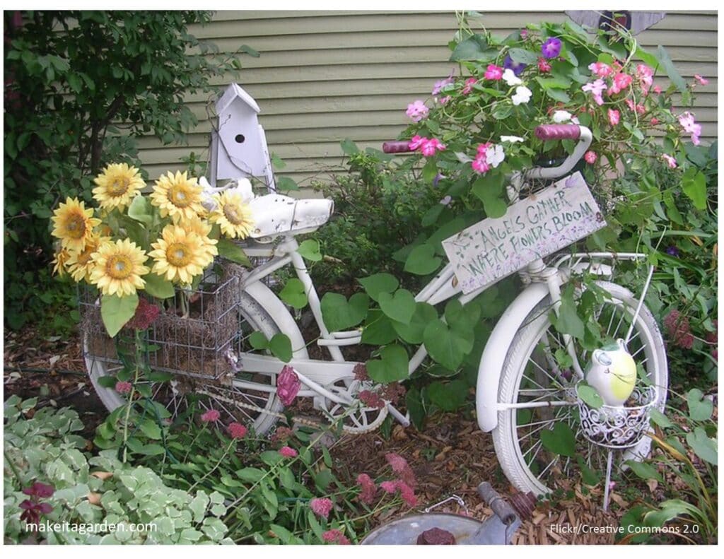 Photo of old bicycle painted white with flower baskets in front and over the back wheel. 