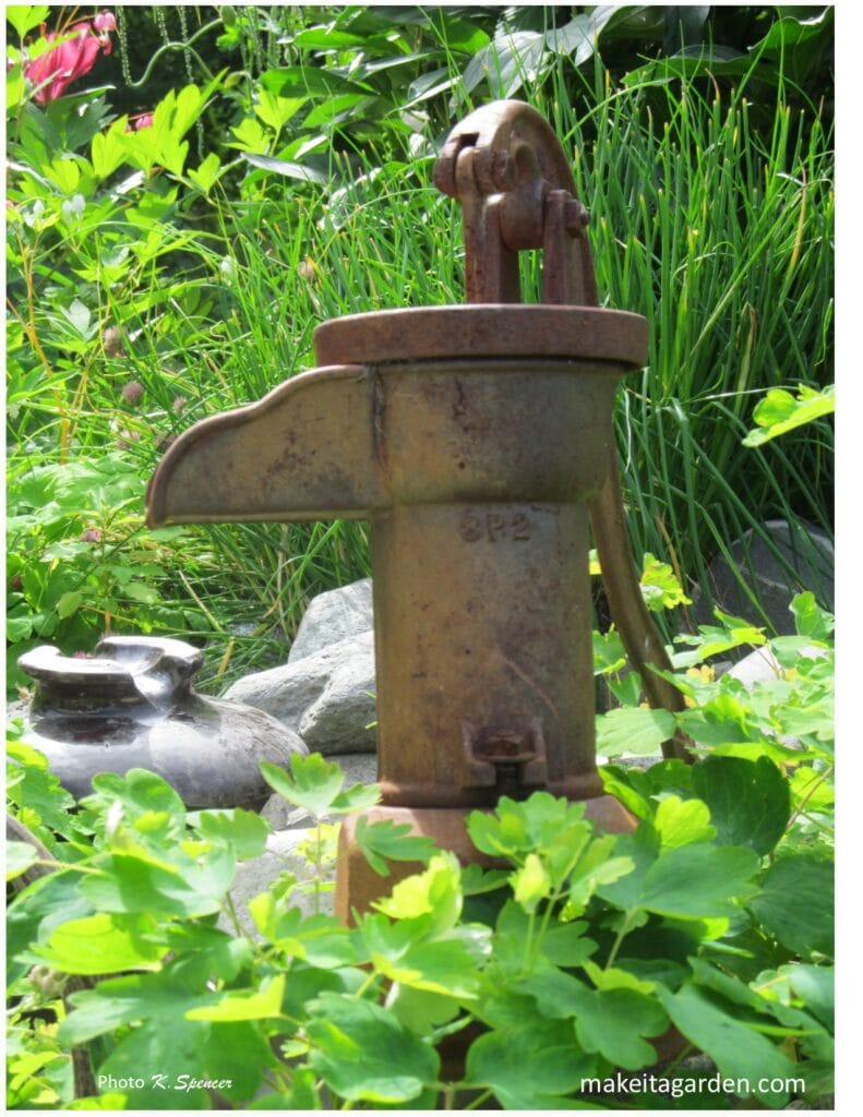 Image of a well water pump head used as art piece in a flower bed. Imaginative sculptures make Palmer Garden