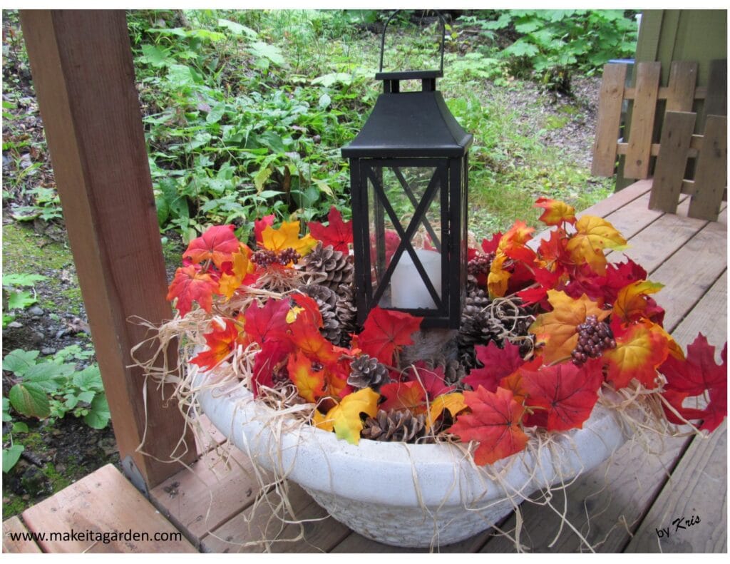 planter filled with leaves and pine cones and straw sticking out around the sides with black candle lantern in the middle Decor for Pretty Fall porch