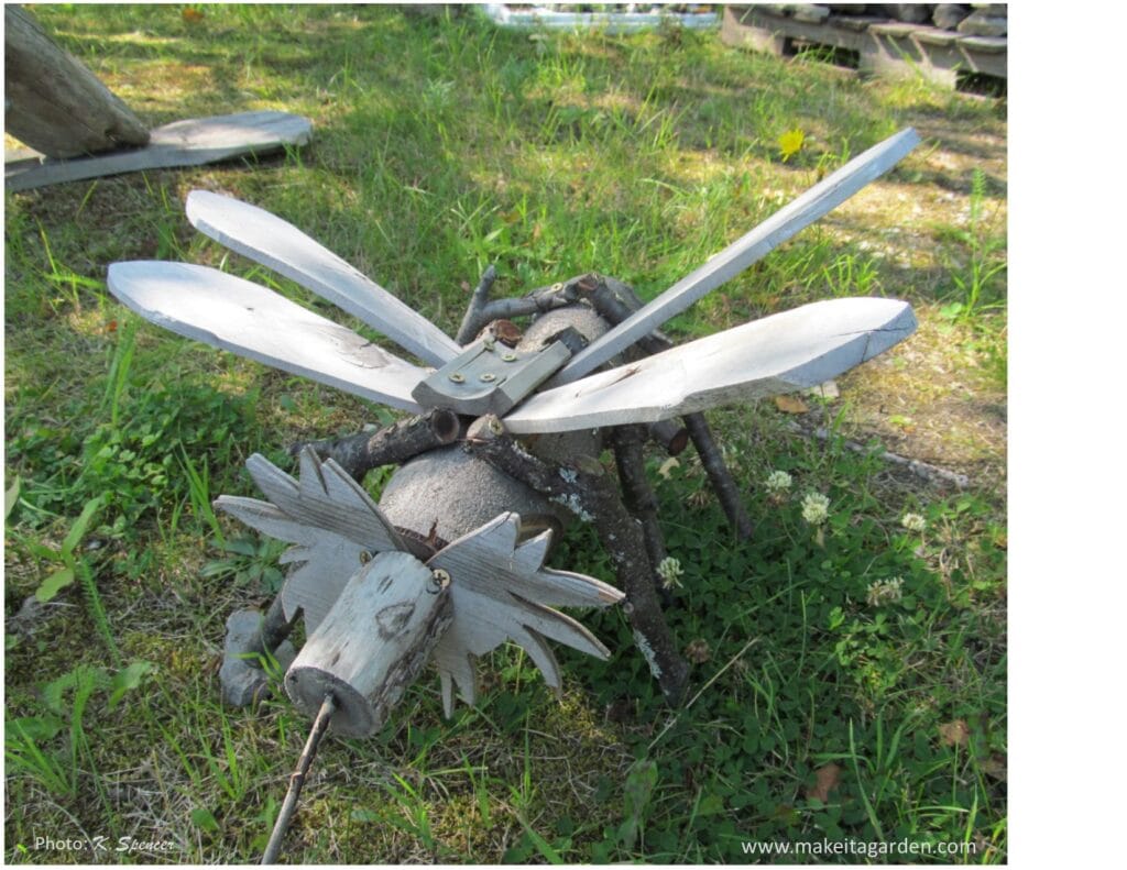 silly driftwood sculpture with the body of a mosquito with wings and a head like a moose with antlers. Driftwood makes a happy garden
