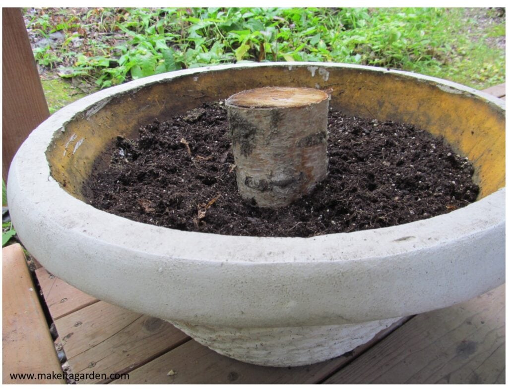 a large, round flower planter with dirt and a short piece of log in the center. 