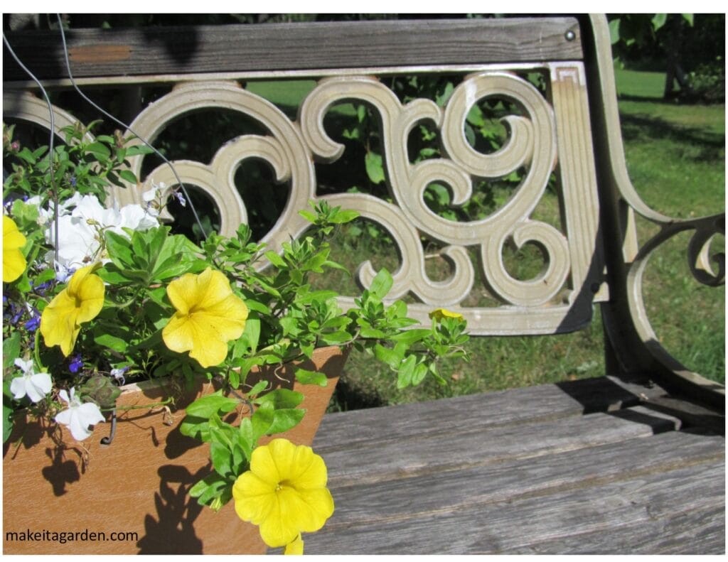 Close up of a wooden park bench and basket of trailing flowers on it.
