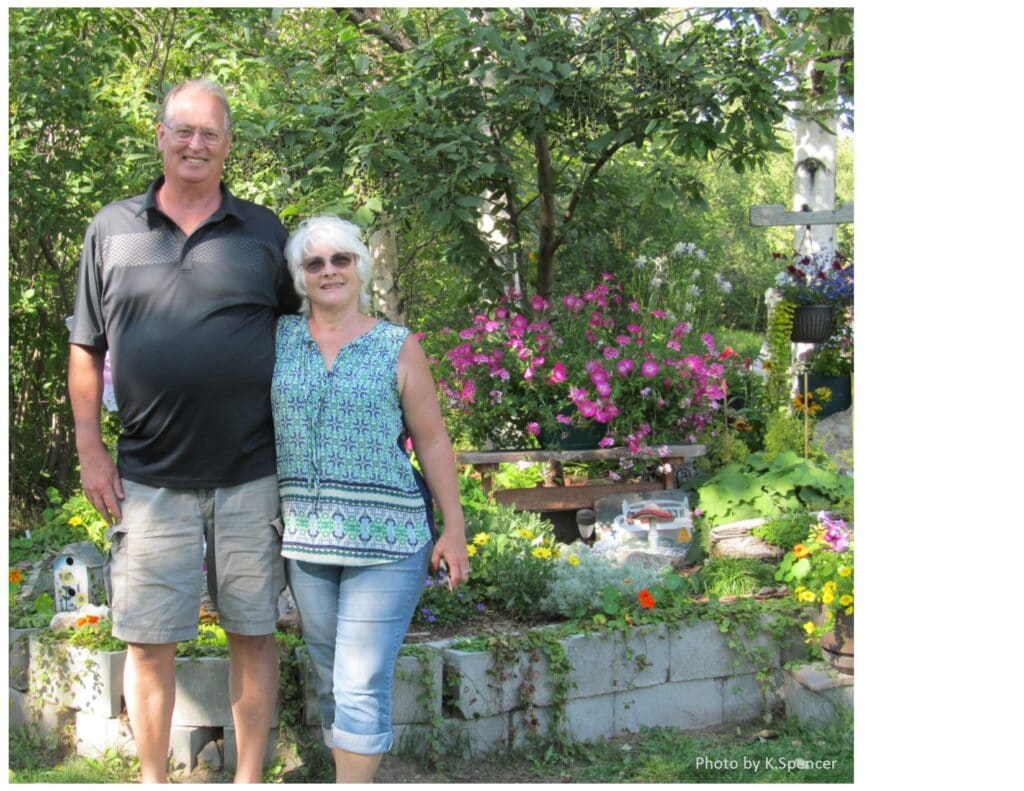 the husband and wife couple who created the garden stand in front of their raised garden full of flowers
