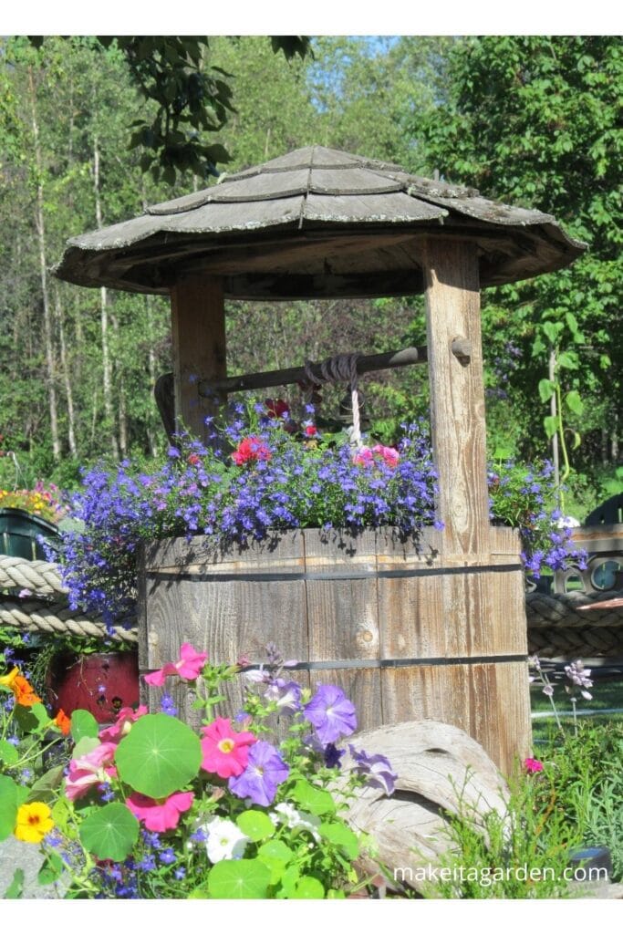 a wood wishing well planter overflowing with flowers in the front yard