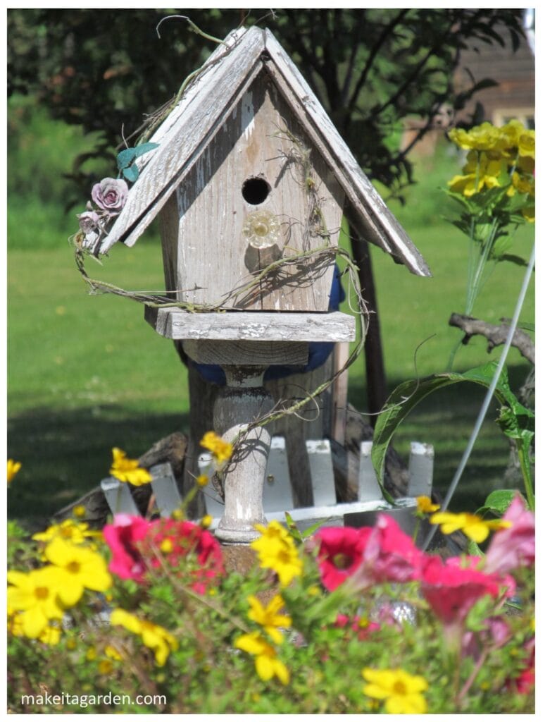 Close up of wooden bird house used as garden decor attached to a post in the garden surrounded by flowers