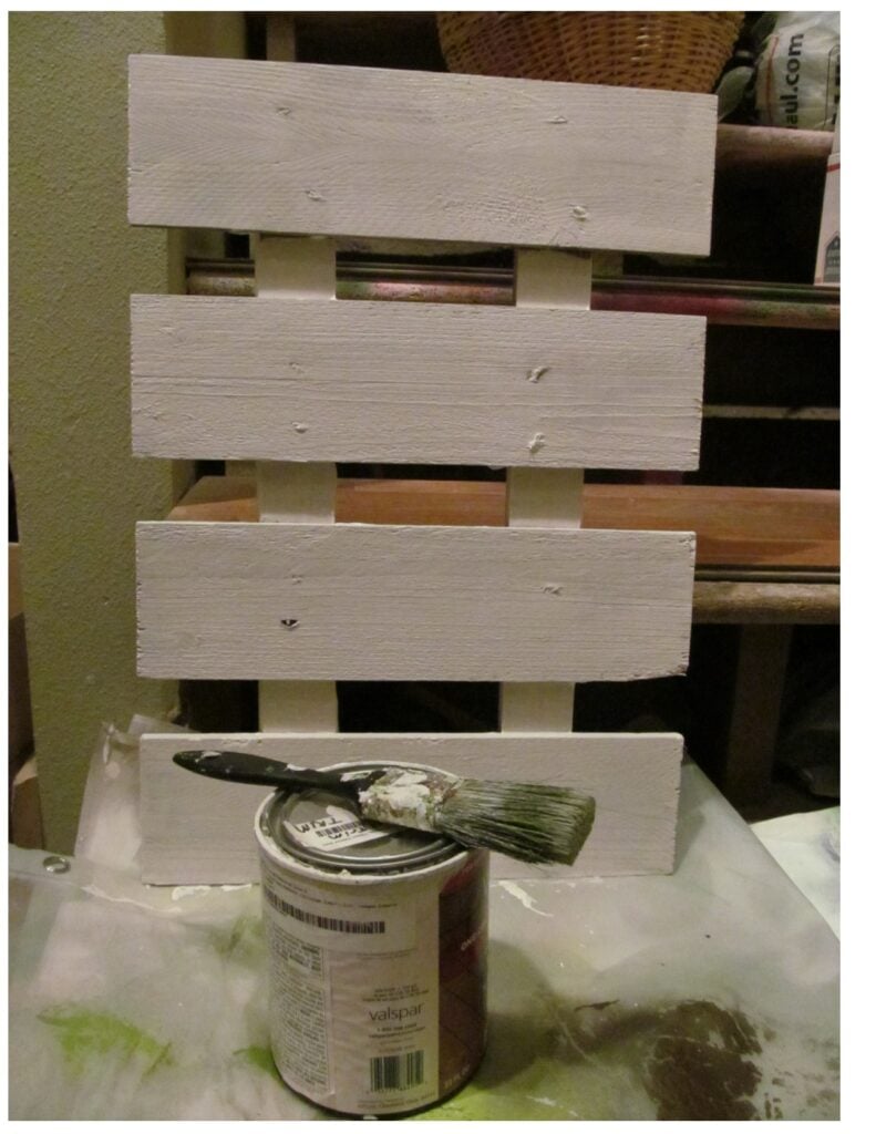 Small wooden pallet painted all white next to a paint can and paint brush