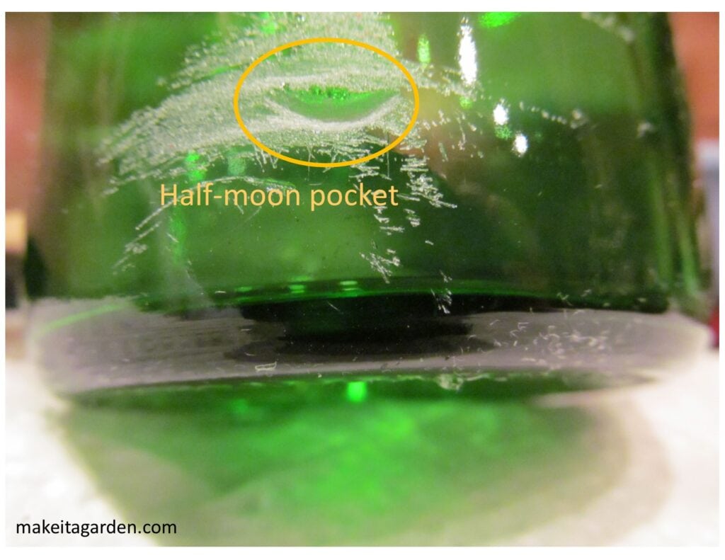 Close up showing the half-moon divot hole made in the glass at the bottom of the bottle. 