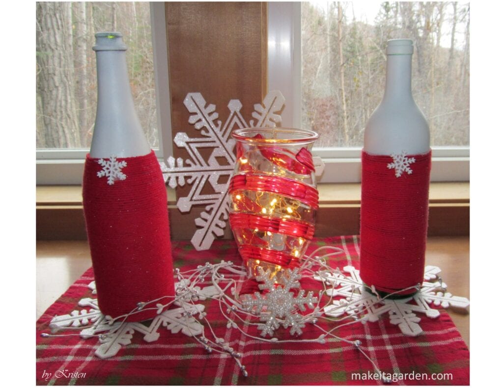 yarn wrapped wine bottles in a table centerpiece with a string of mini lights and plastic snowflakes