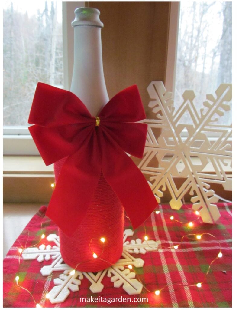 yarn wrapped wine bottle with a big red bow on it in a festive display