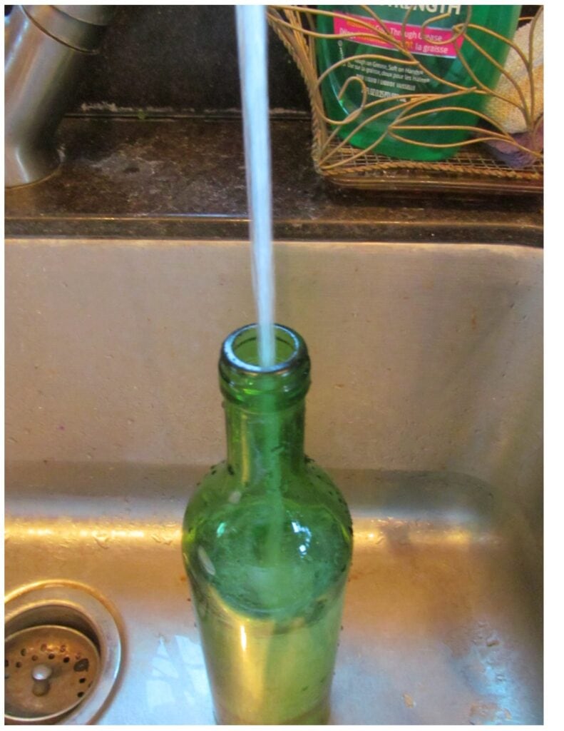 a wine bottle under a faucet in the sink getting filled up with water