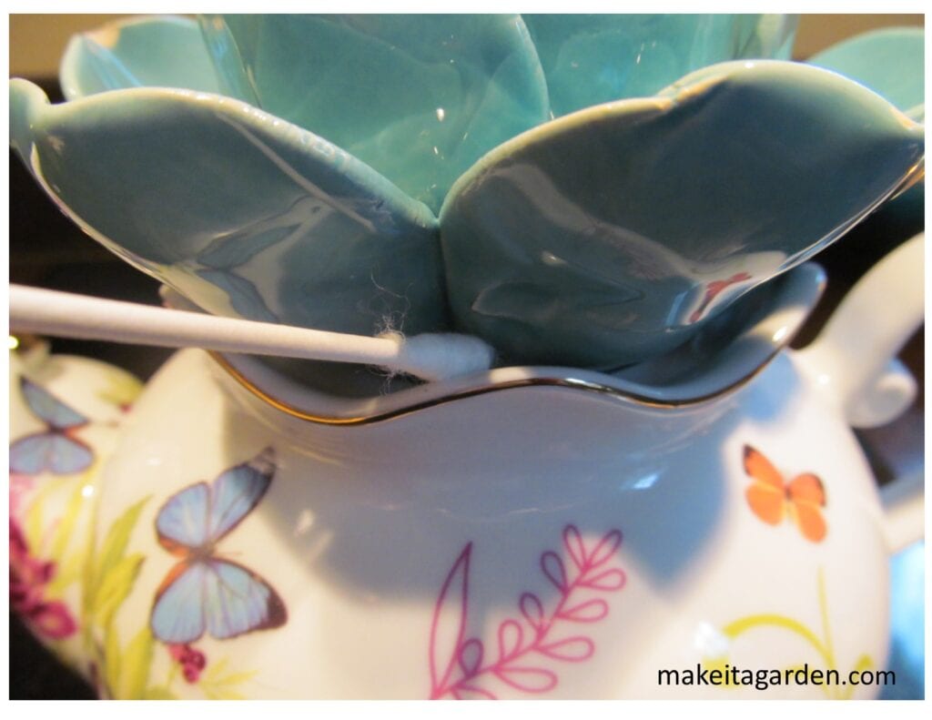 close up of applying silicone glue with a Q-tip to glue teapot and ceramic flower together