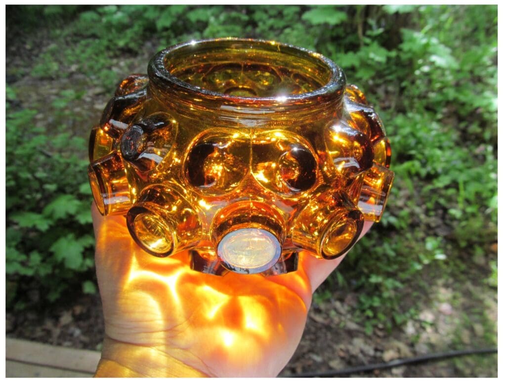 a short, small round amber-colored glass vase with unique design of bubbles on the side of it. 