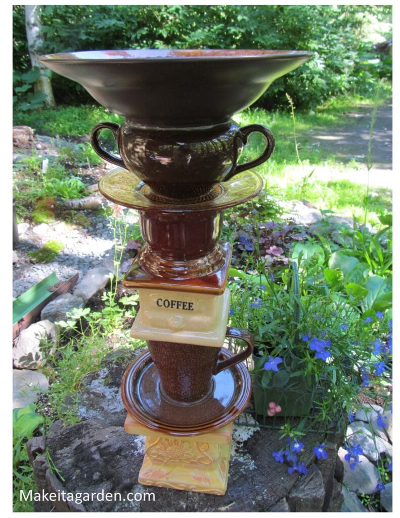 a coffee themed totem sculpture comprised of brown colored dishes, a flower vase in the shape of a coffee grinder and a coffee mug.