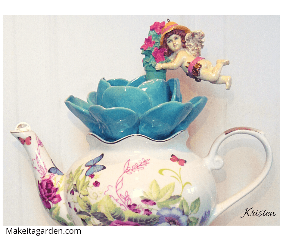 Close up of the pretty teapot, with ceramic flower on the top of it and a little fairy figurine on the flower.