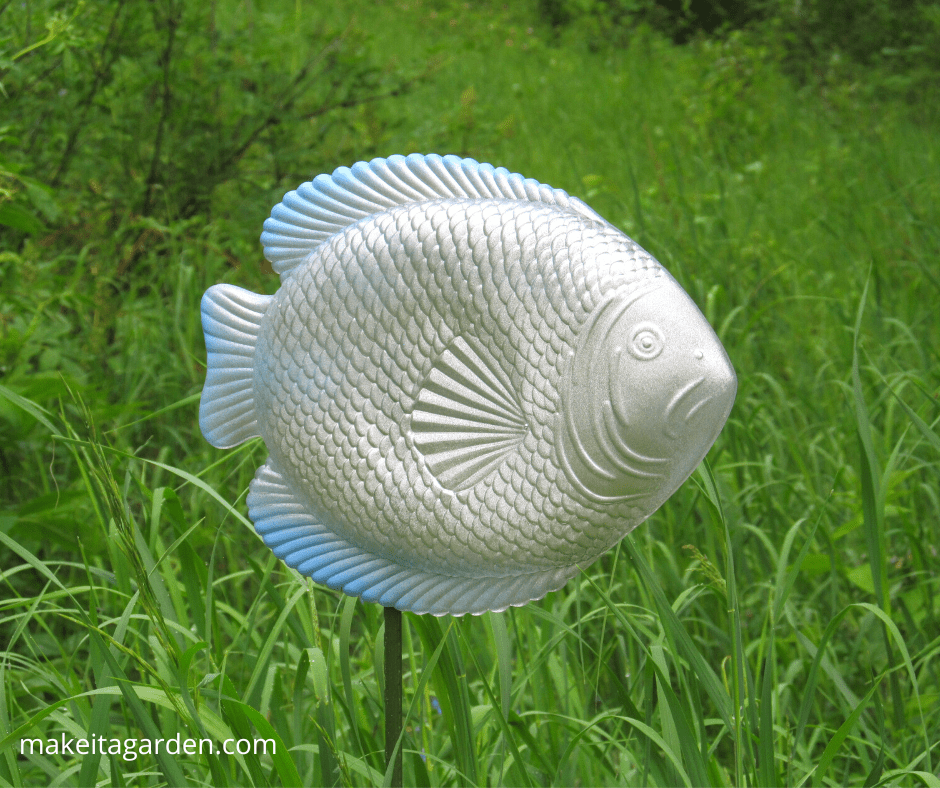 plastic fish spray-painted with silver metallic paint "swims" through tall grass