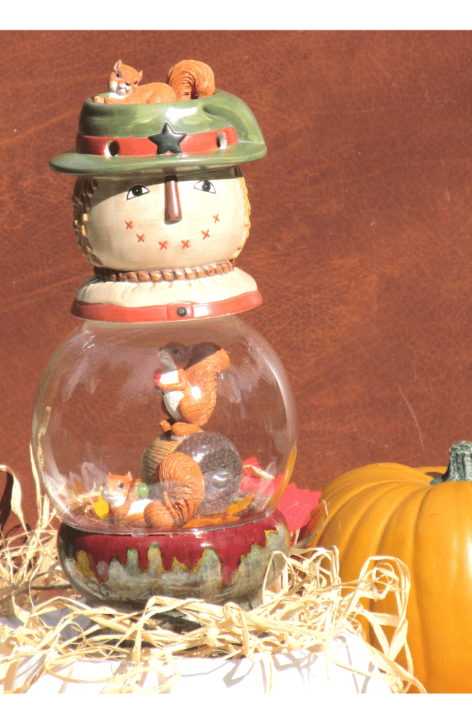 glass globe scarecrow craft is displayed on straw next to a pumpkin