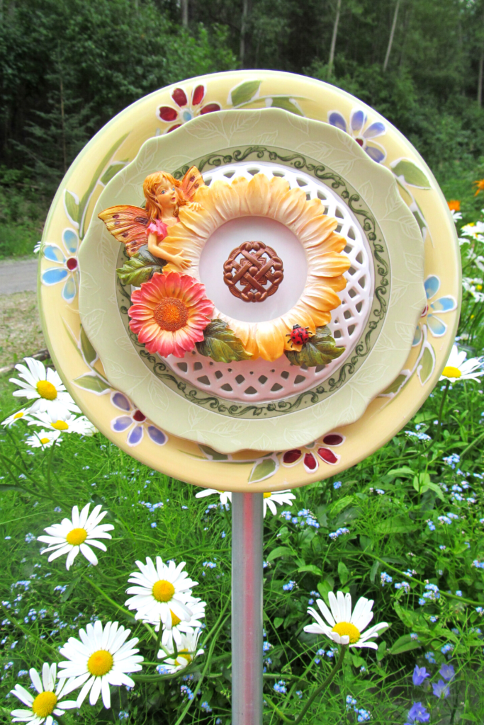 Ceramic plates put together to look like a garden art flower. In the center is a sunflower with a darling little fairy.