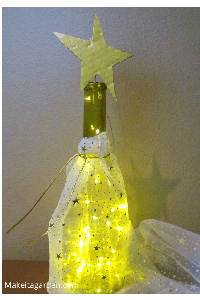 Clear glass wine bottle wrapped with sheer sparkly fabric and a star on top