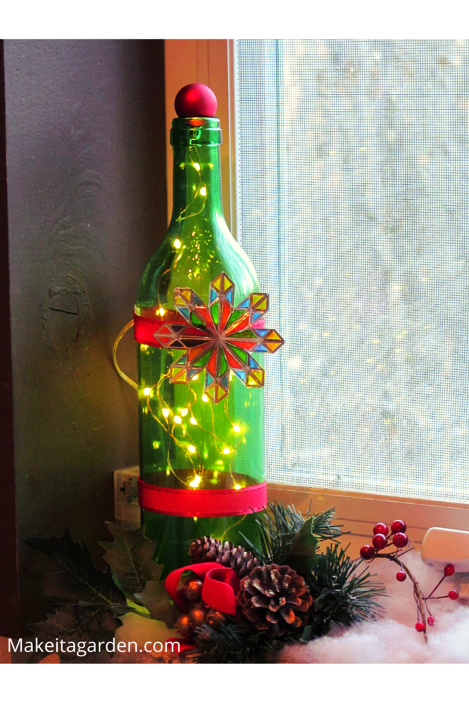 Green glass wine bottle trimmed with ribbon and small tree ornament filled with mini lights. An idea to decorate a wine bottle.  